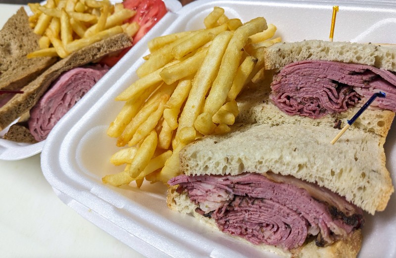 A takeout container of corned beef sandwiches and fries.