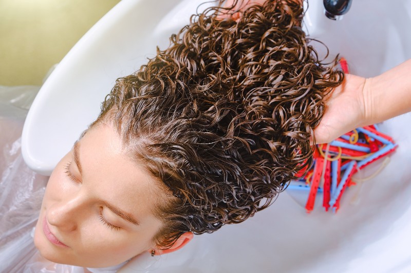 A young woman with long curly hair receives a wash and cut
