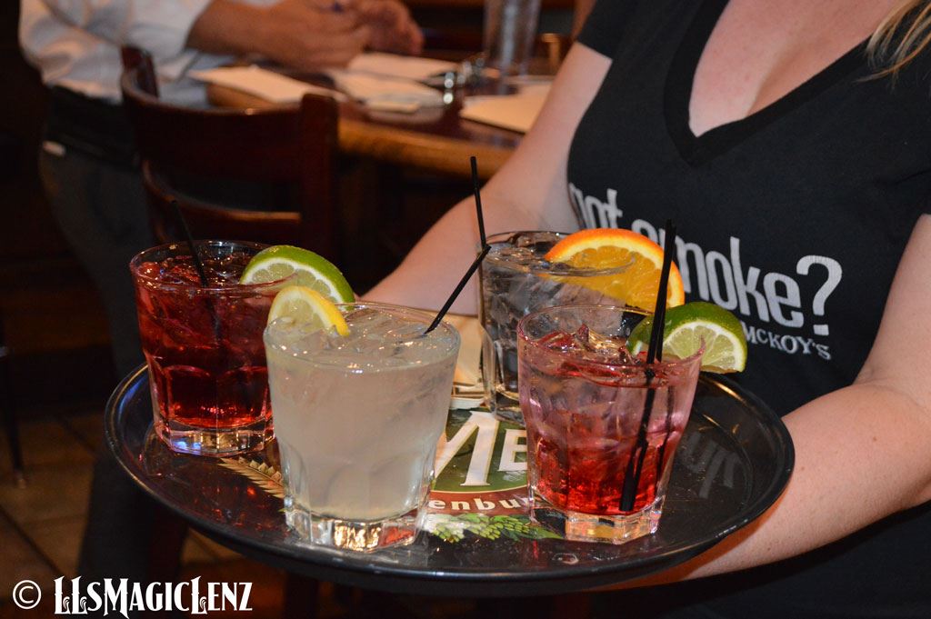 A tray of drinks on a platter is carried by a waitress.