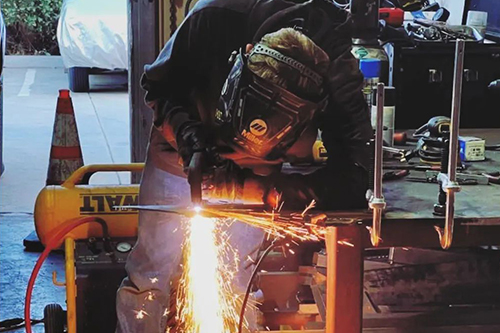 A welder performs a welding job with a large array of sparks falling to the floor.