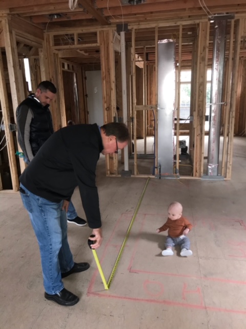 Workers measure a room while a toddler looks on