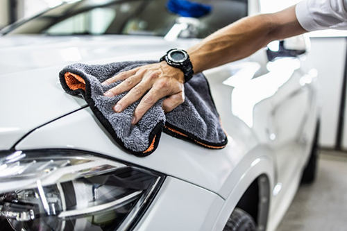 A man buffs a white car’s front end.