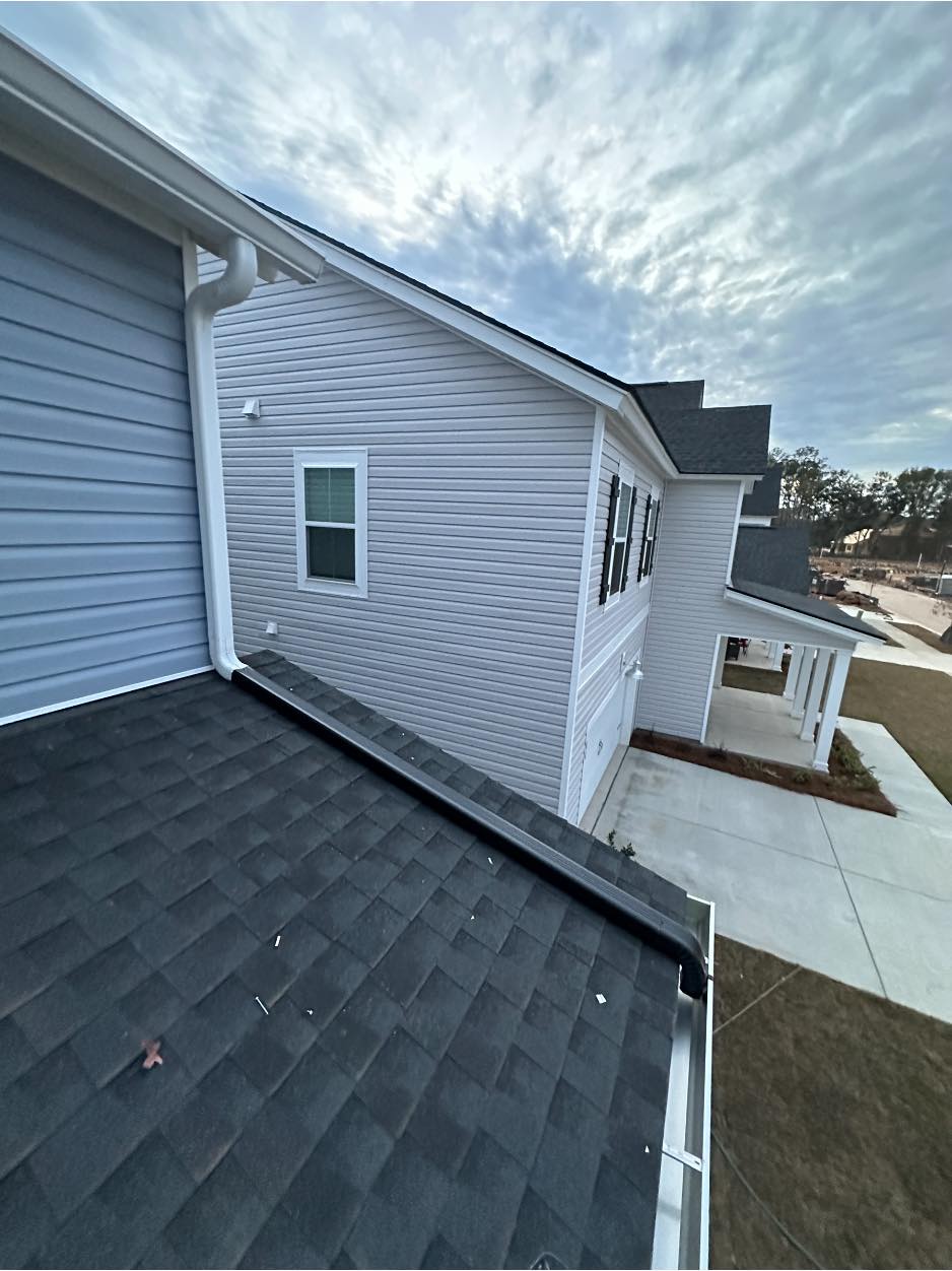 A gutter with a long drain spout extending across the lower-level roof of a home.