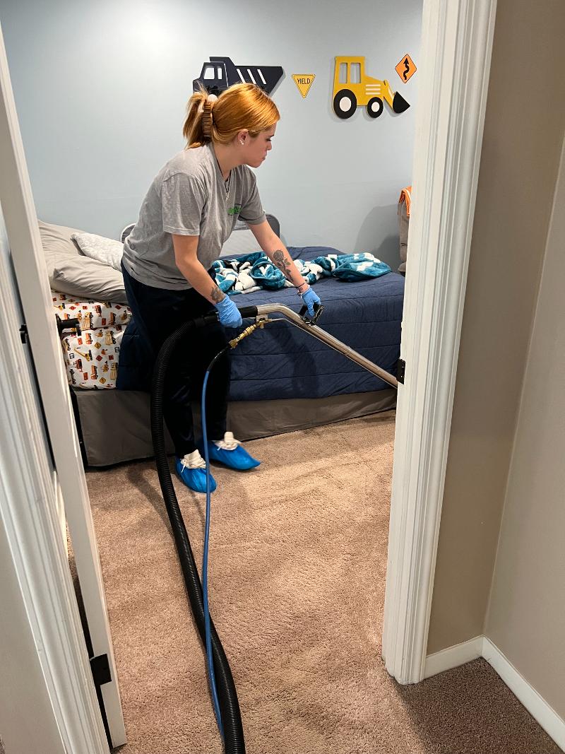A woman steam cleans the carpeting in a bedroom.