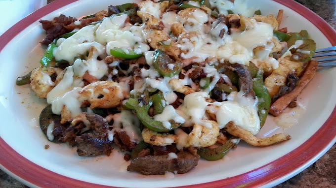 A plate of steak and chicken strips with peppers covered in a queso sauce.