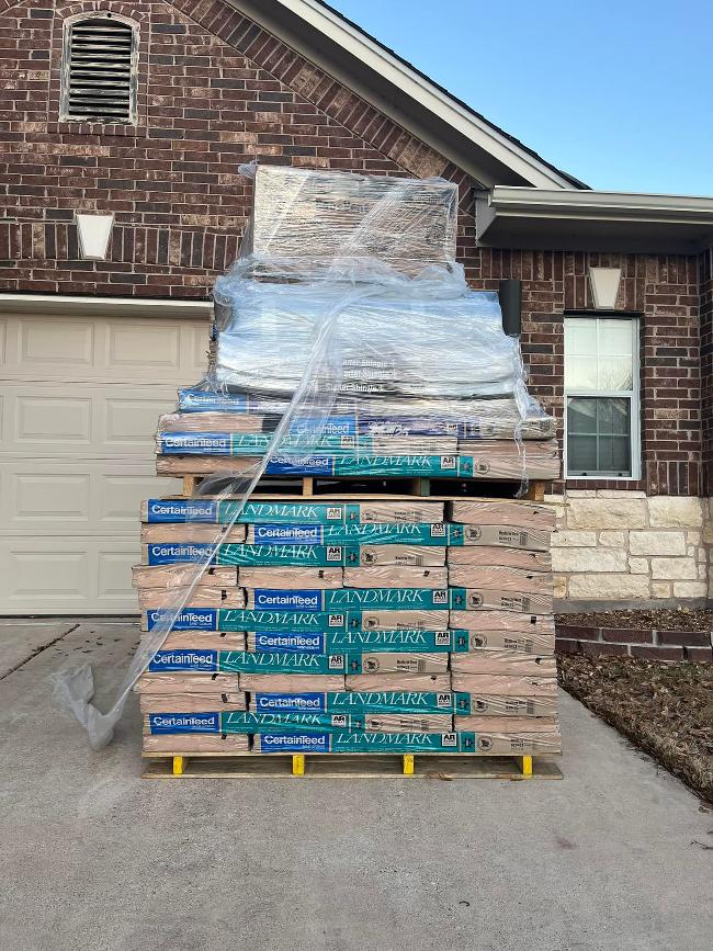 Stacks of Landmark shingles sit on a pallet in the driveway of a home.