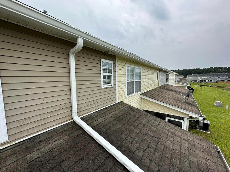 A gutter with a long drain spout extending across the lower-level roof of a home.