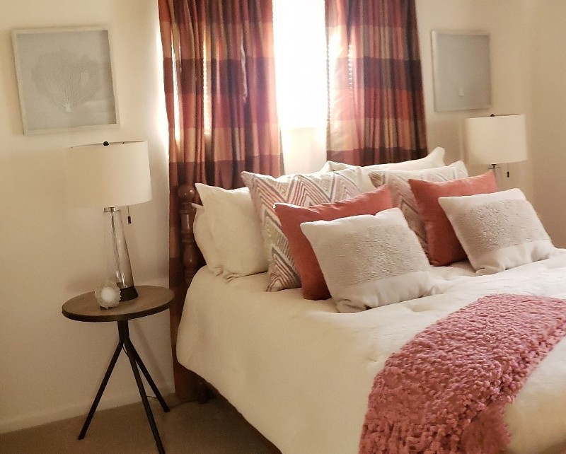 A comfortable bedroom with tan carpeting and deep red curtains.