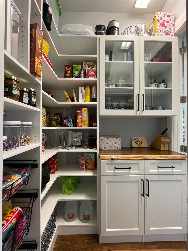 A pantry with two sections of open shelving filled with items with pantry doors to the right and glassed doors on top.