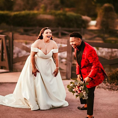 A bride and groom laugh with the groom holding a bouquet.