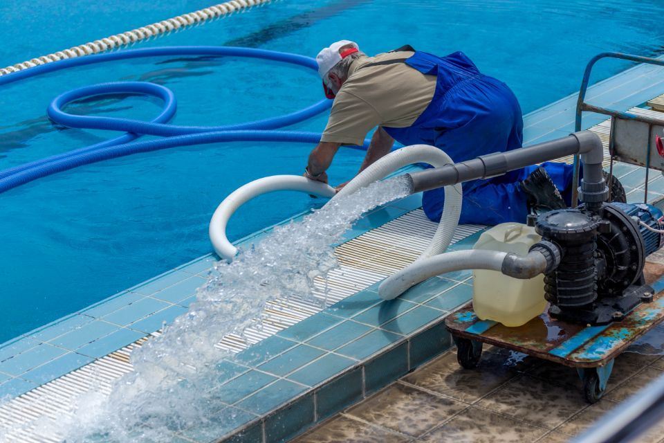 A man inserts hoses from a pump system into a pool.