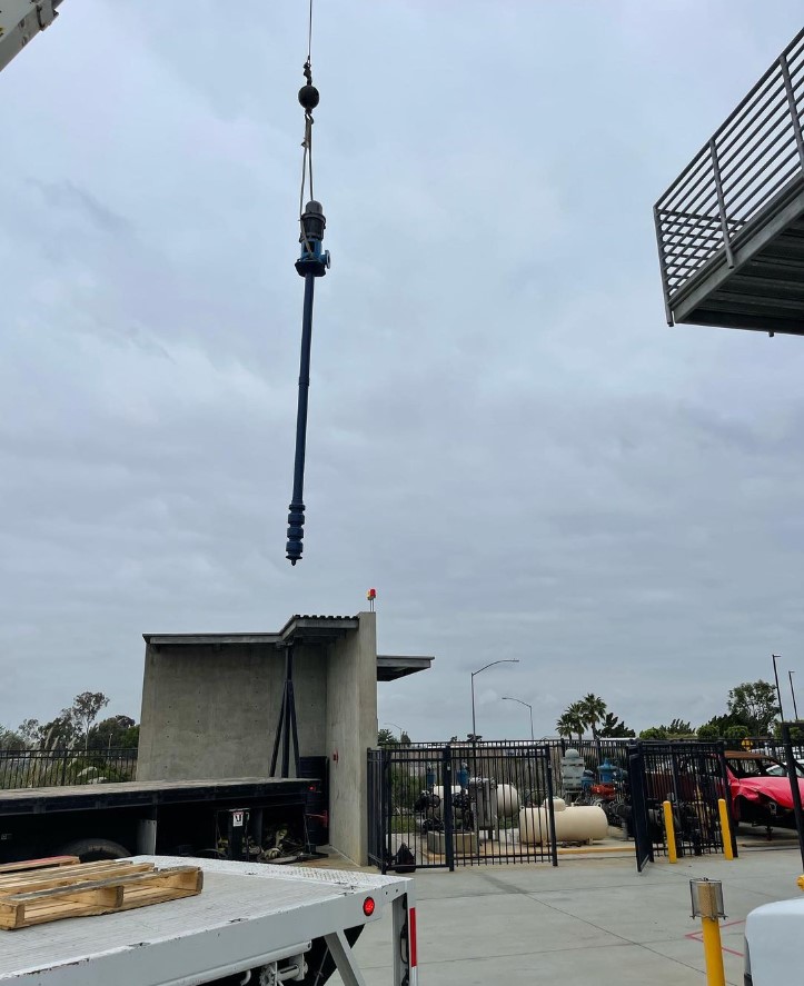 A long, thin piece of equipment is lowered into place by a crane.