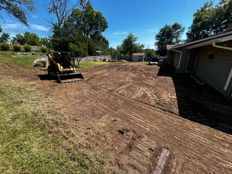 A skid loader sits in a leveled strip of land.