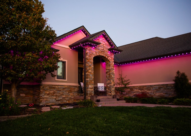 Trimlight lighting set to pink on a brown home.