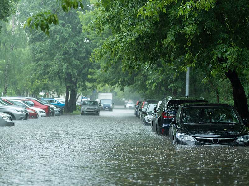 Rows of cars on either side of a roadway sit in high water during a pouring rain.