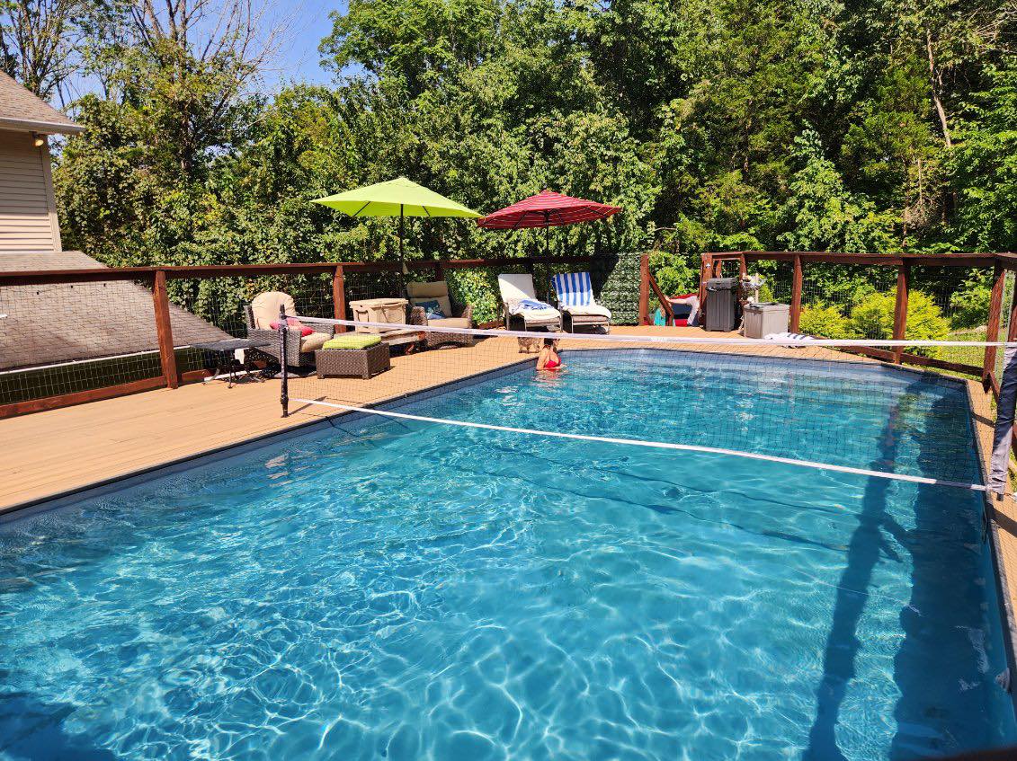 Above-ground backyard pool surrounded by a pool deck with a volleyball net stretched across the middle.