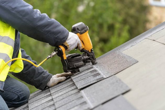 Crew member using a nail gun to lay roof shingles.