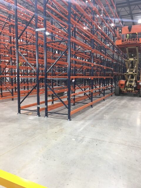 A scissor lift raises its lift to the top level of racking in a warehouse.
