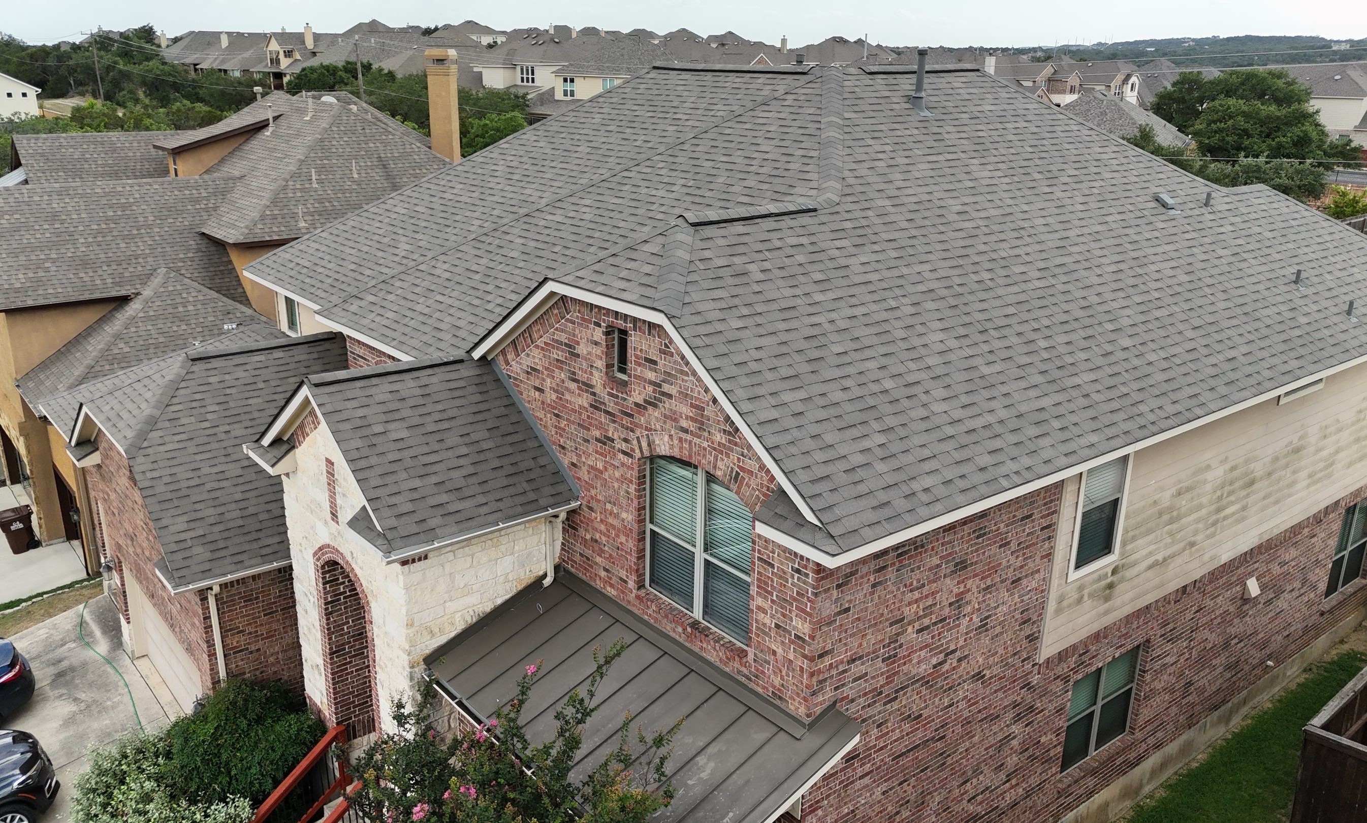 The overhead view of a large home of many sections with gray shingle roofing.