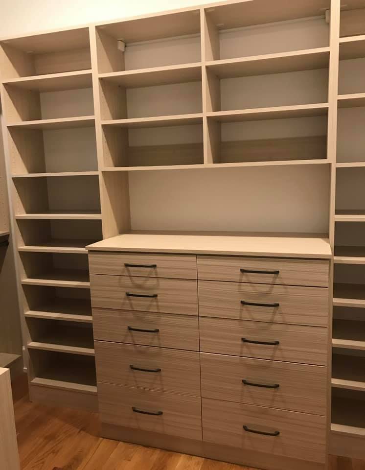 A wall of open-shelf storage with a section of drawers in the middle at the bottom.