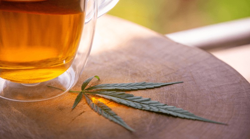 Cannabis leaf on a wooden stool next to a cup of tea