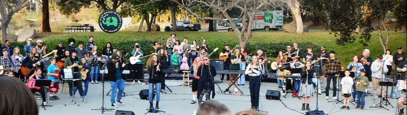 A large group of musicians and singers outside on a concrete stage.