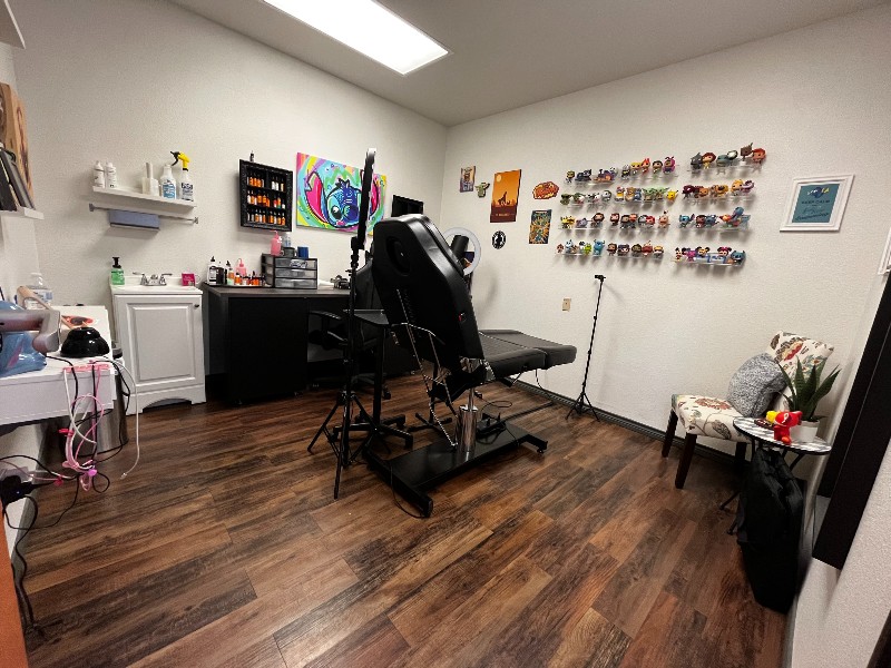 a tattoo parlour with dark wood floors, a black chair, designs and inks adorn the walls