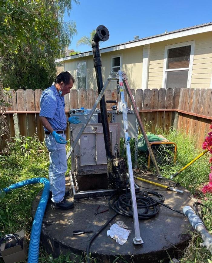 A man stands over a round septic system observing pumping taking place.