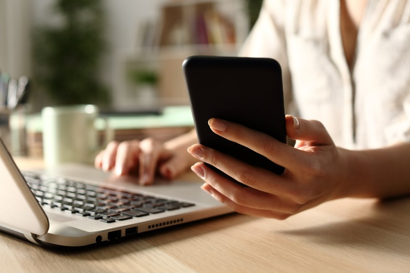 A woman looks at her cellphone with her laptop computer in front of her.