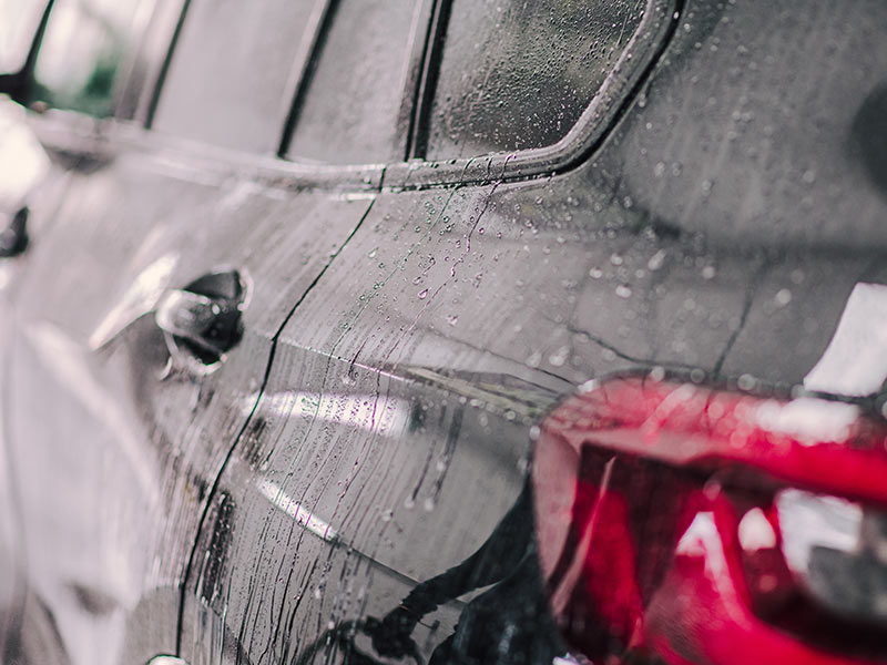 The side view of a car from the rear fender is seen while rain falls.