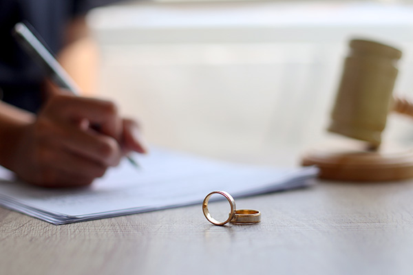 Woman's hand signing papers with wedding rings in the foreground
