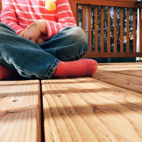 A boy sits on a floor of wooden planks.