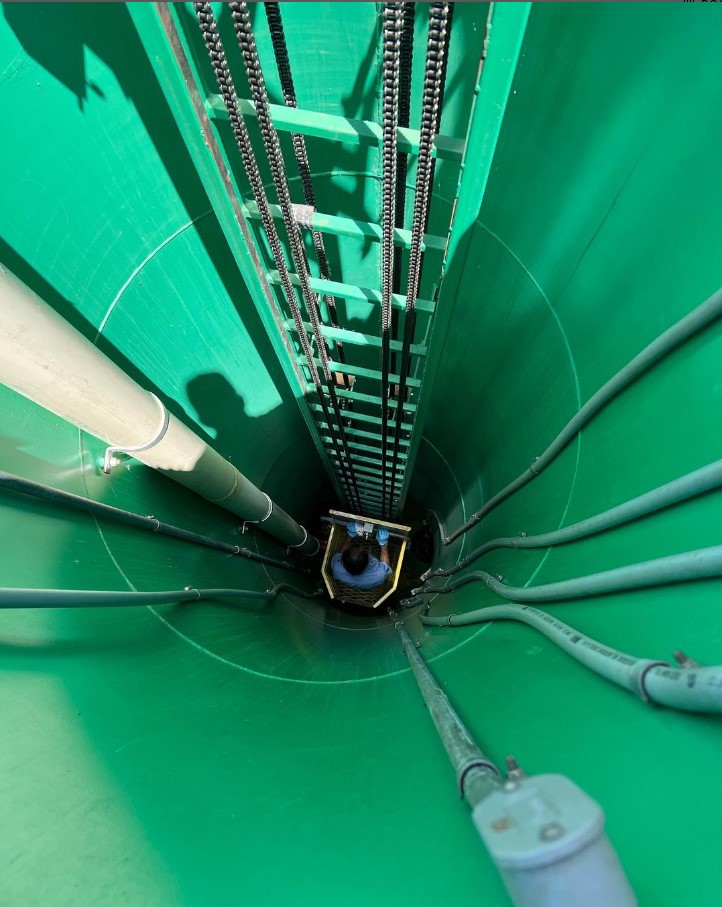 A ladder leads down a green chute with electrical conduit.