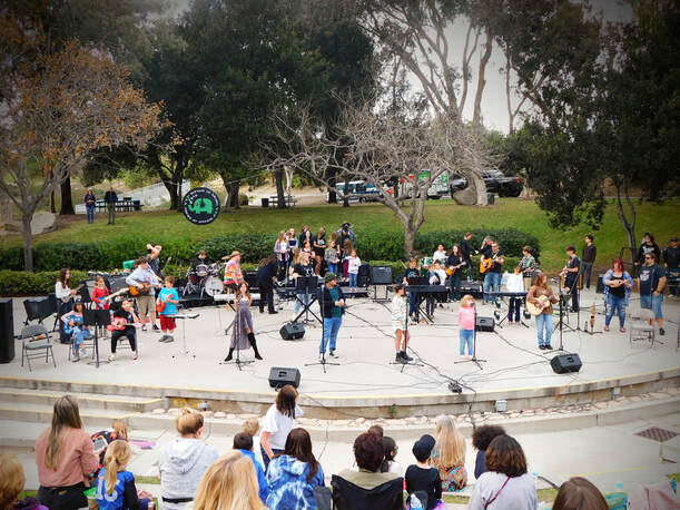 A large group of musicians and singers outside on a concrete stage.