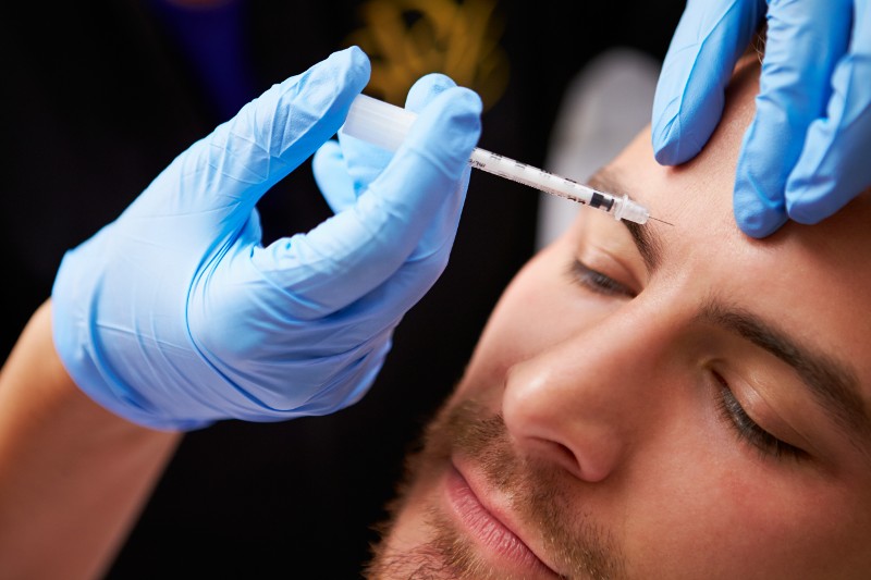 A man takes an injection from a syringe into his forehead.