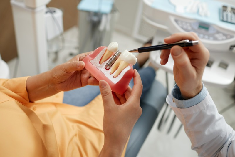 Close-up of senior woman holding tooth model during consultation on dental implant surgery in dental clinic