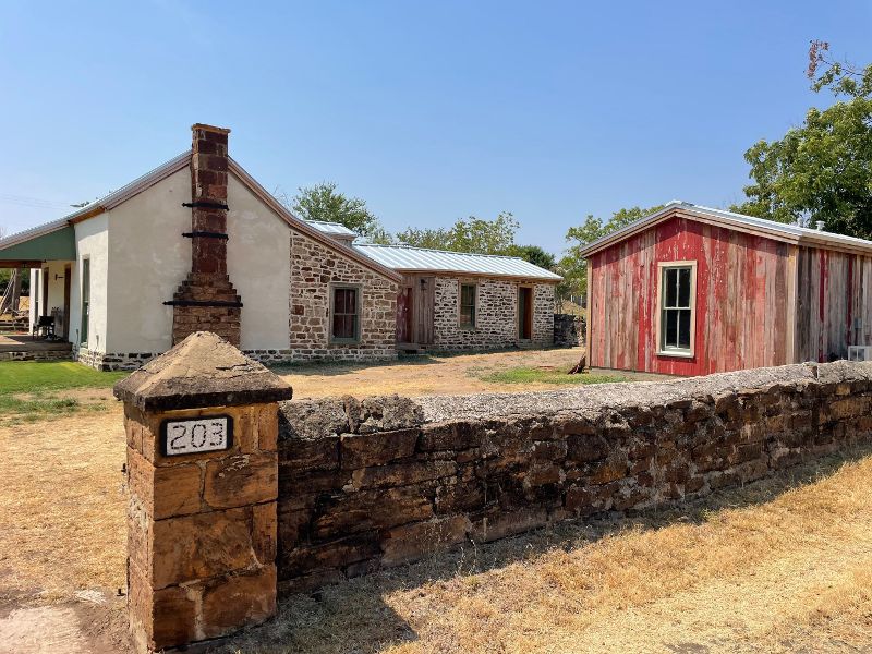 An older home sits beyond a stone fence and small red shed.