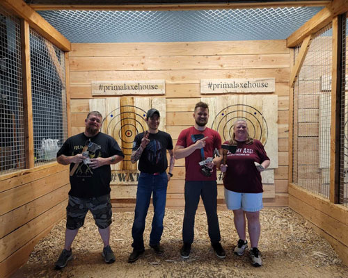 Four axe throwers pose for a photo in a throwing lane.