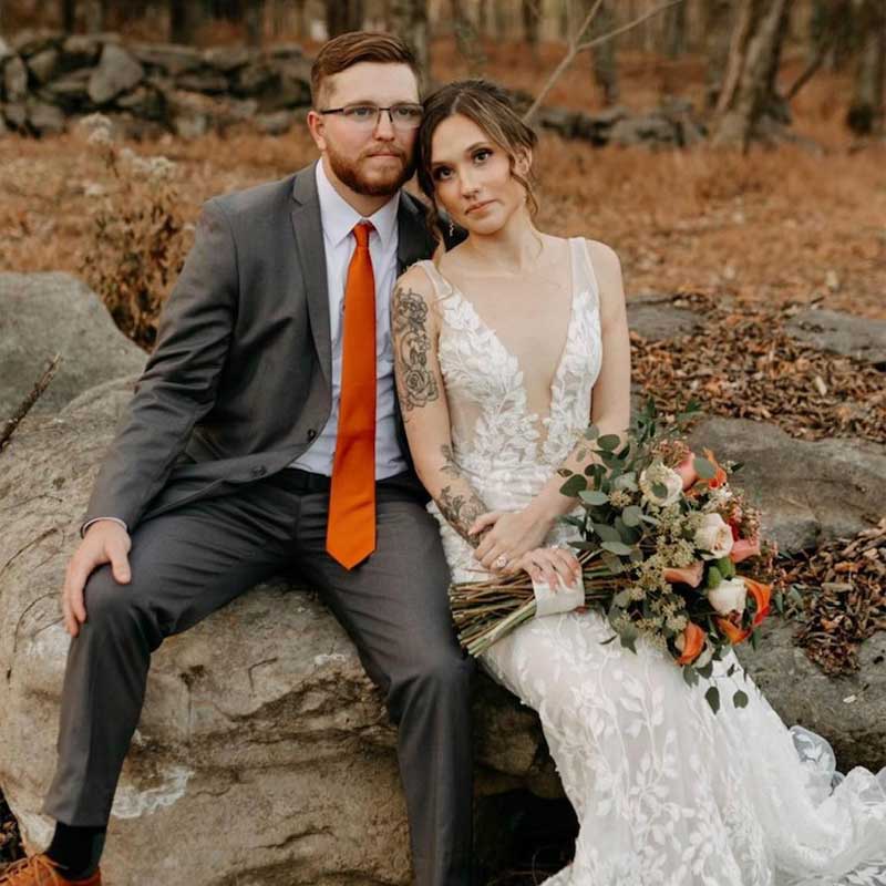 A wedding couple poses for a photo while sitting on a large rock.