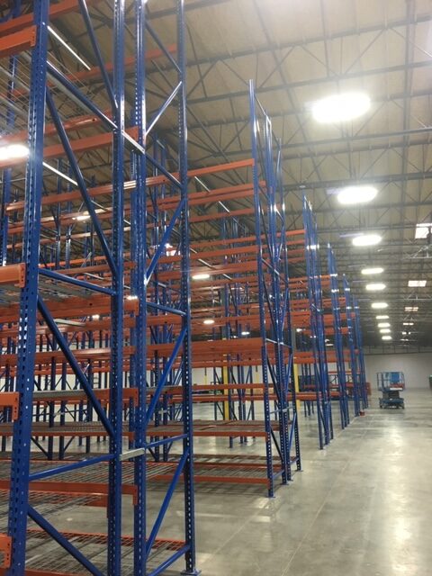 An open aisle next to rows of multi-tier racking systems in a warehouse.