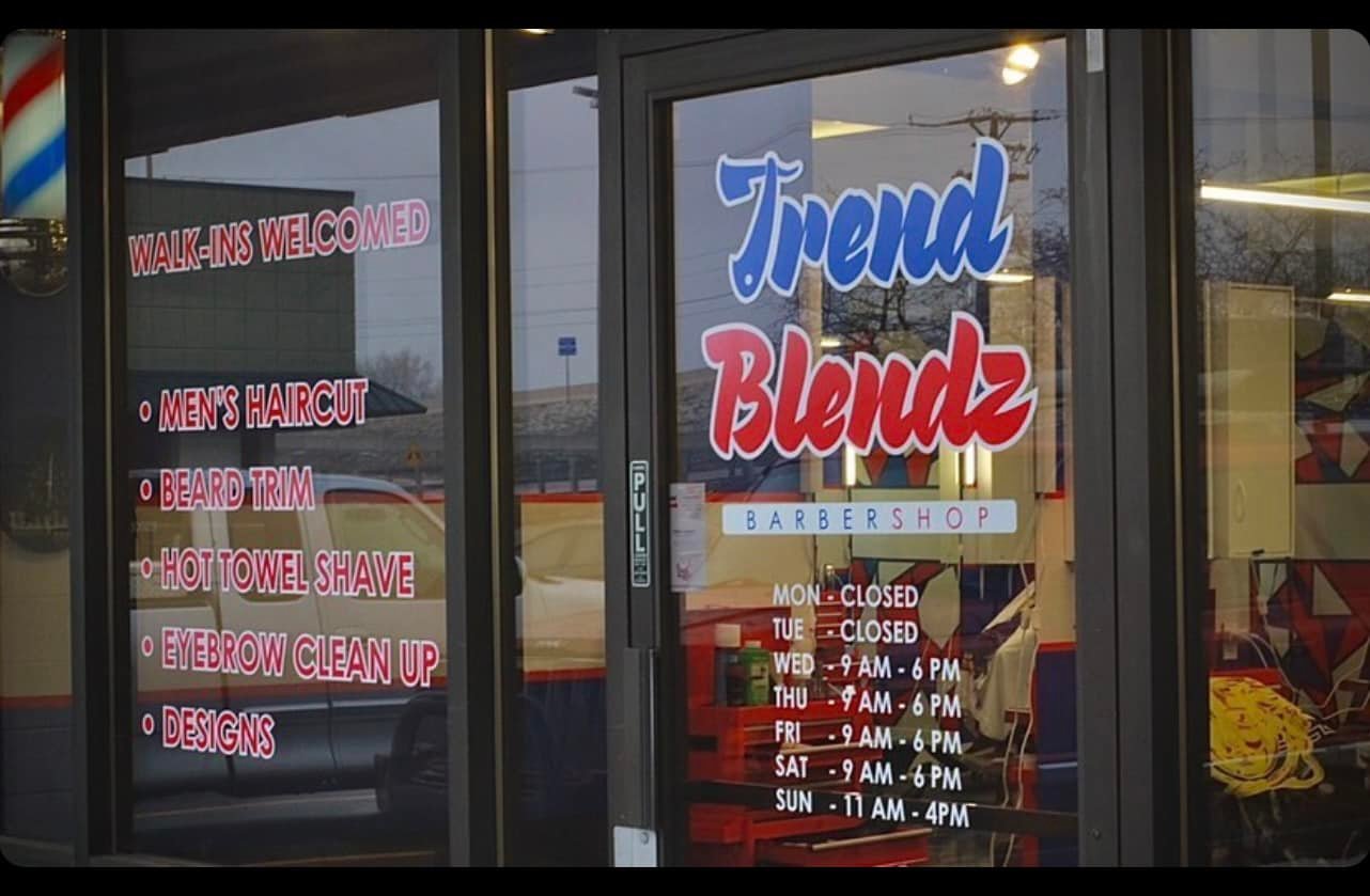 The outside windows of the Trend Blendz Barbershop shows their hours and list of services. 