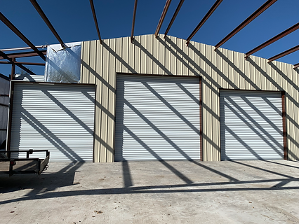 Three white metal roll-up doors of various sizes on a beige warehouse building.