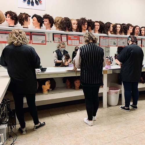 Three beauty school students work with wigs.