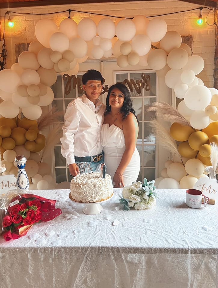 A bride and groom pose behind their wedding cake.