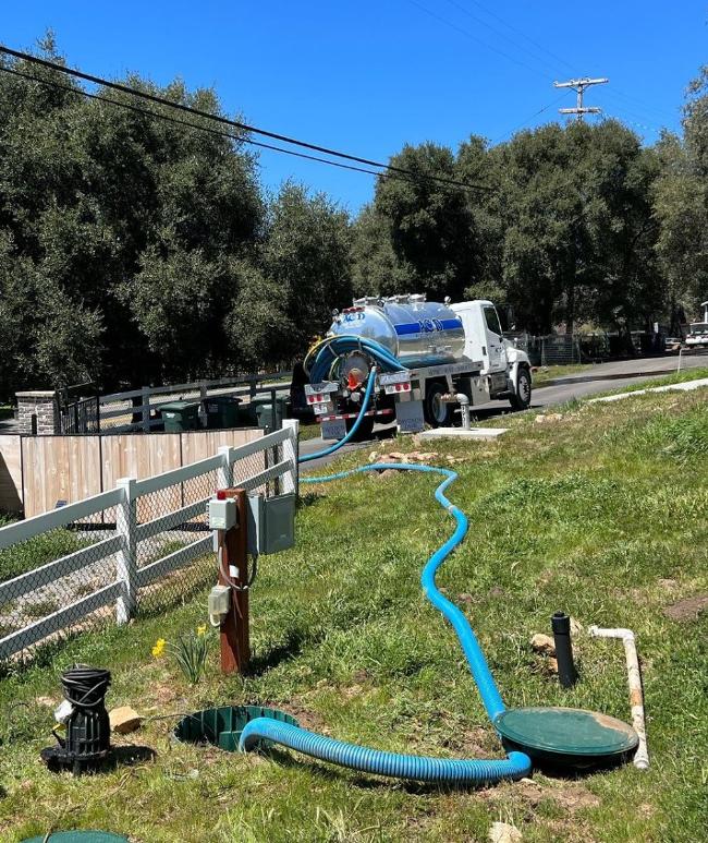 A pumper truck has a long, blue hose leading into a septic system.