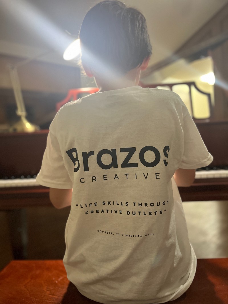Young boy in a Brazos Creative t-shirt playing piano.