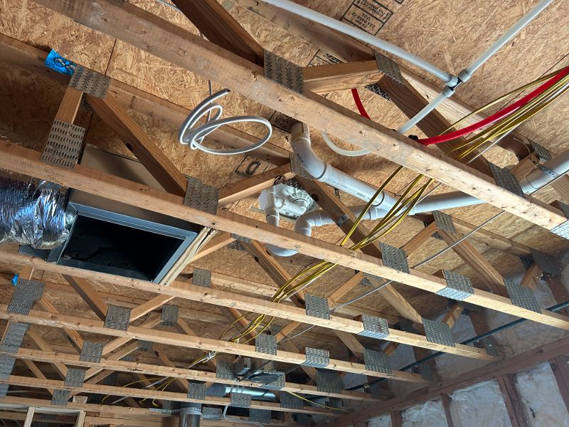 Looking up at piping and wiring installed into an open ceiling.