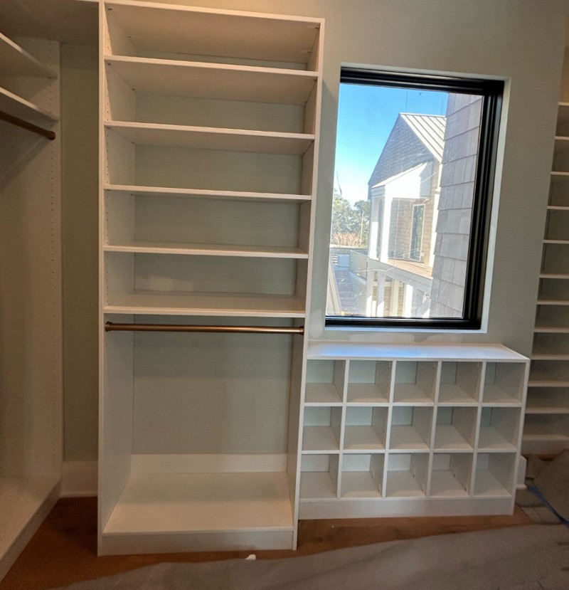 The corner of a room with open shelving and a window over an open shoe storage.
