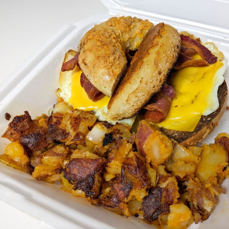 A bacon and cheese bagel sandwich with hash browns.