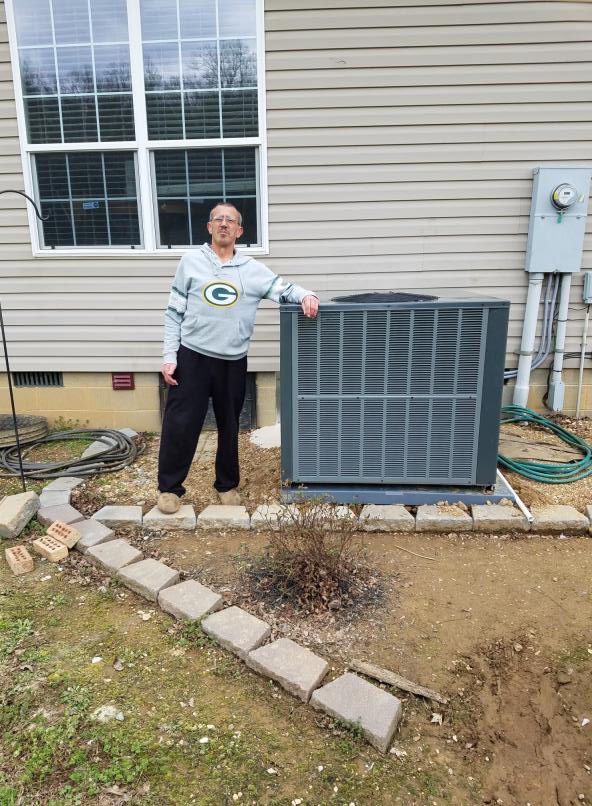 A man stands next to an outdoor HVAC unit.